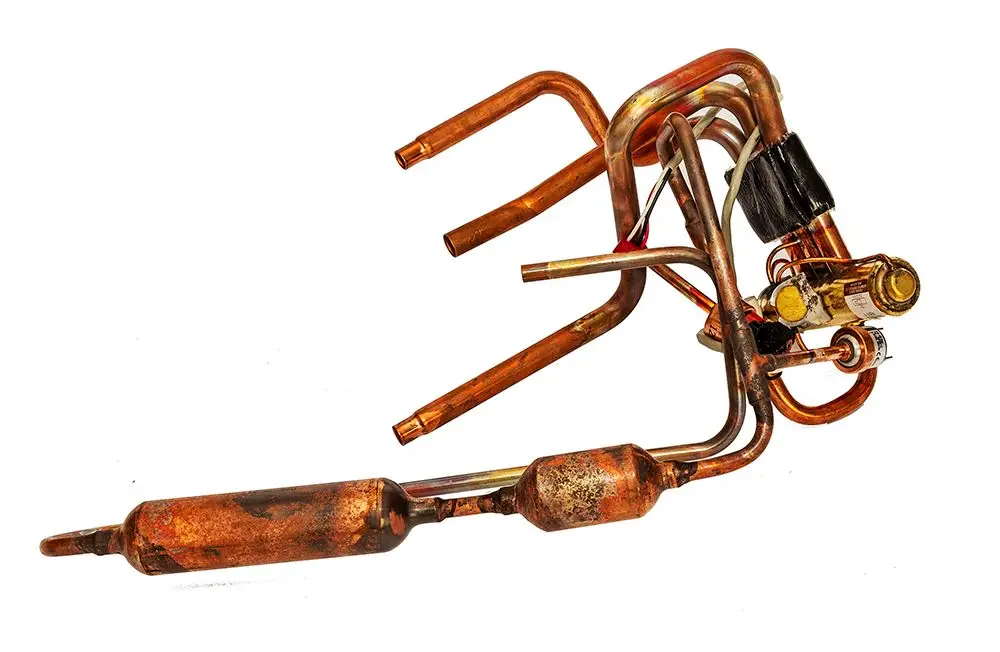 Daikin 4-Wege-Ventil aus Kupfer mit mehreren Rohren und einem eingebauten Kompressor. Sichtbare Anschlussstellen und unterschiedliche Rohrdurchmesser.